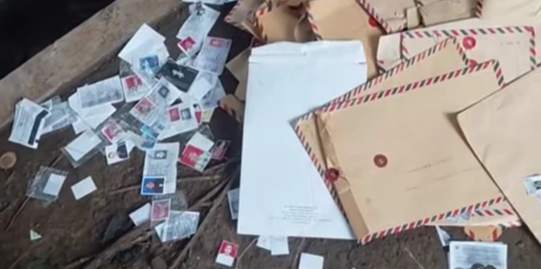 Foto close-up tumpukan amplop coklat lamaran kerja berserakan di pinggir jalan aspal, beberapa terbuka memperlihatkan dokumen di dalamnya.