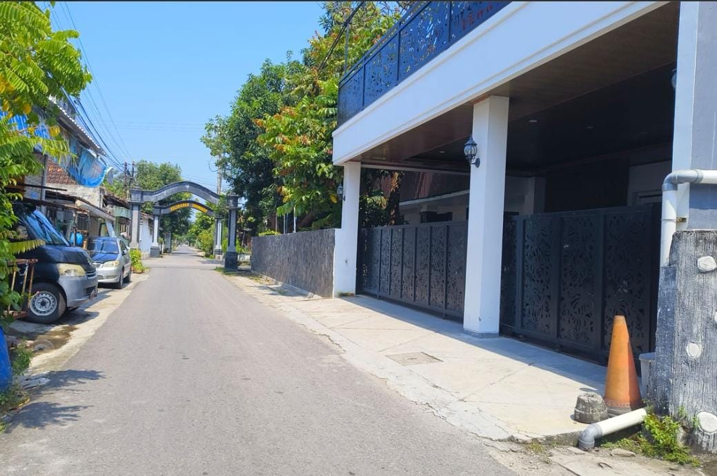 Rumah putih dengan pagar besi dan tanaman hias di depan, tampak sepi.
